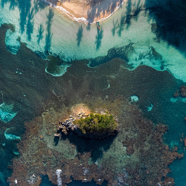 Aerial view of a tropical beach with coral and a boat at the waters edge.