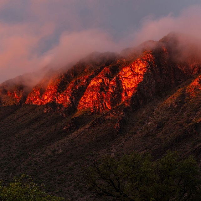 clouds forming on a rocky mountain face at sunrise.